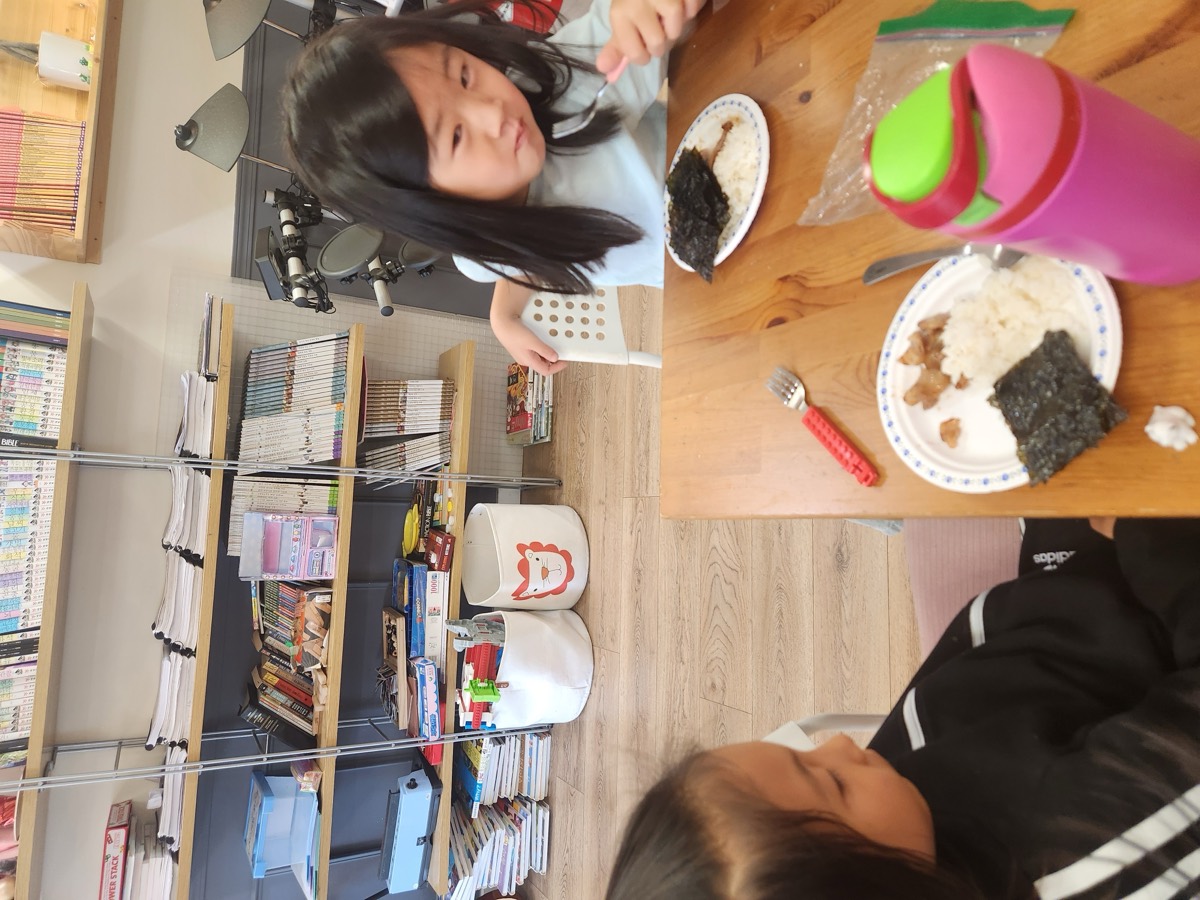 Two children having lunch together at a table by the bookshelf