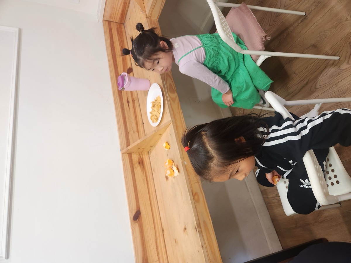 Two children eating a snack while sitting on little chairs