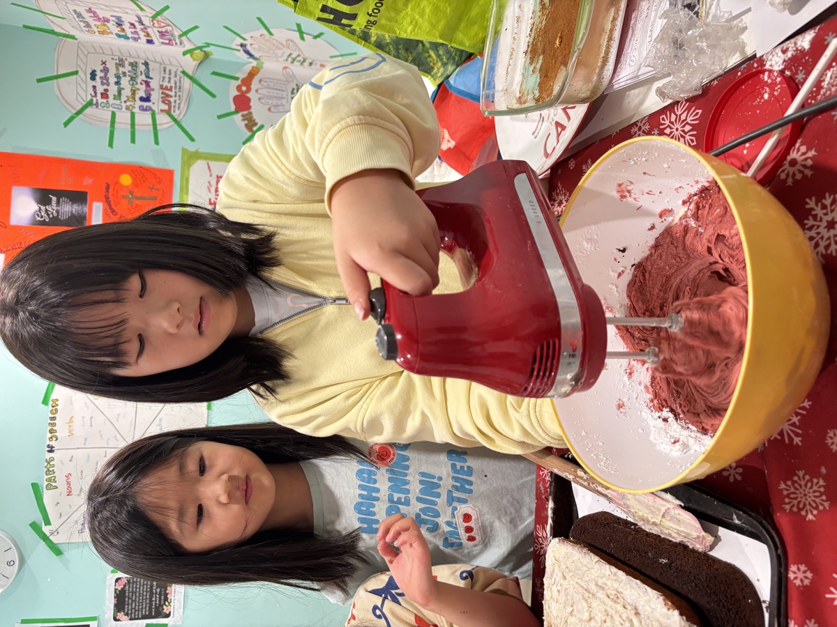 Two girls whipping red velvet batter with a hand mixer