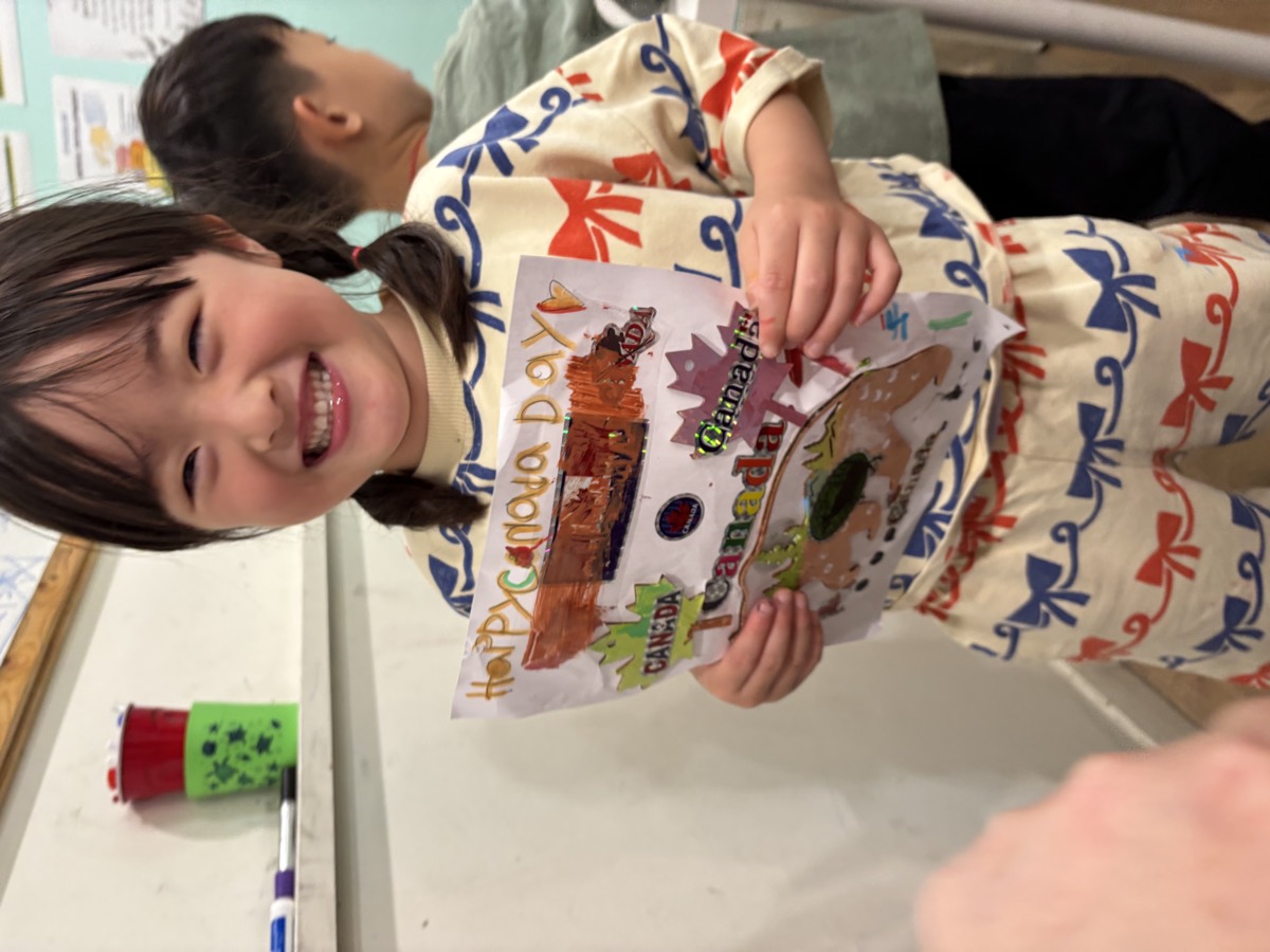A girl beaming while holding her Happy Canada Day drawing