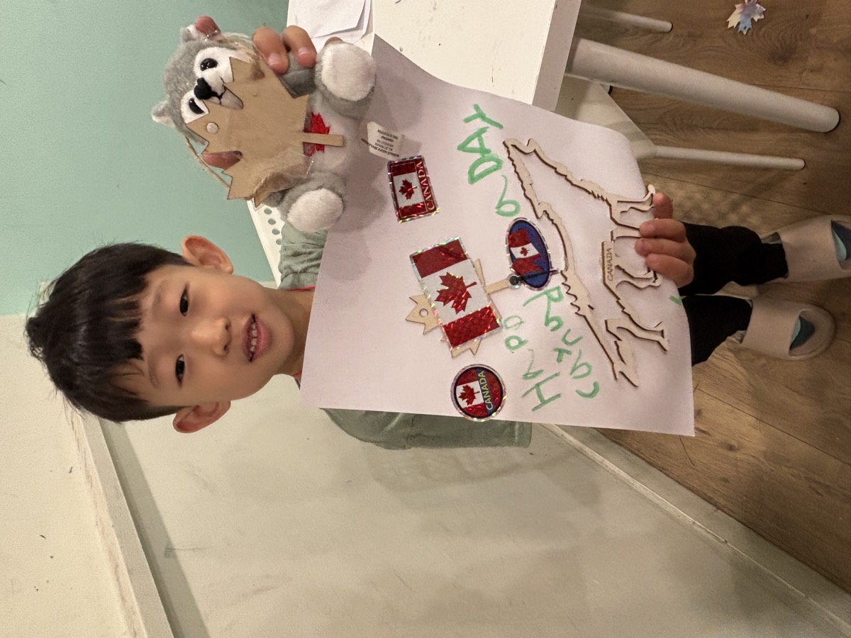 A boy holding his Canada Day poster and a husky plushie