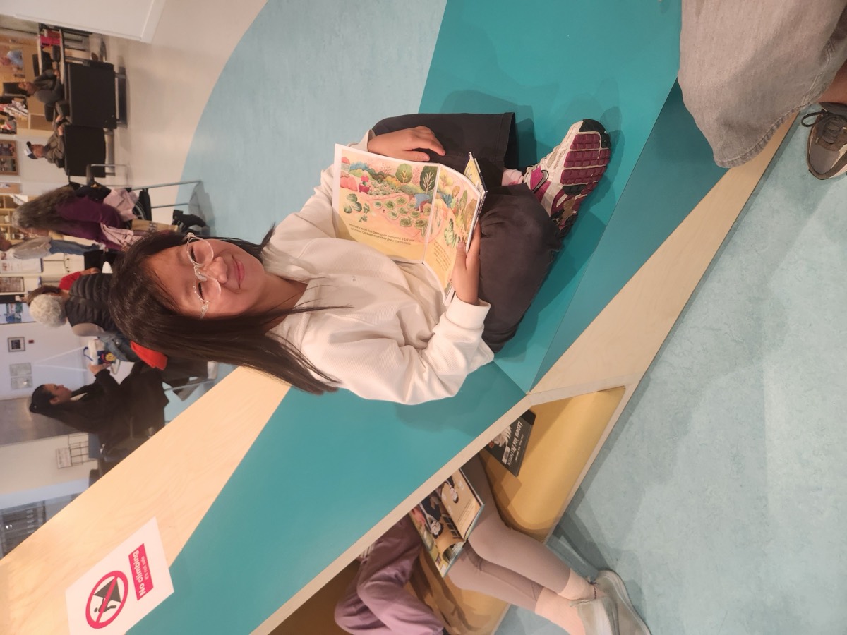 A teacher smiling while reading a picture book in the library