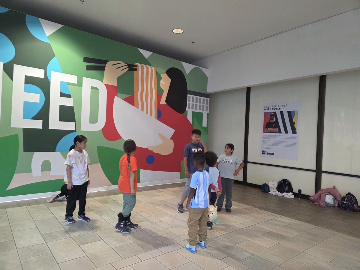 Children standing in front of a large colorful wall mural