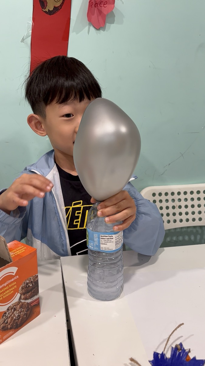 A boy grinning as a balloon inflates on a bottle