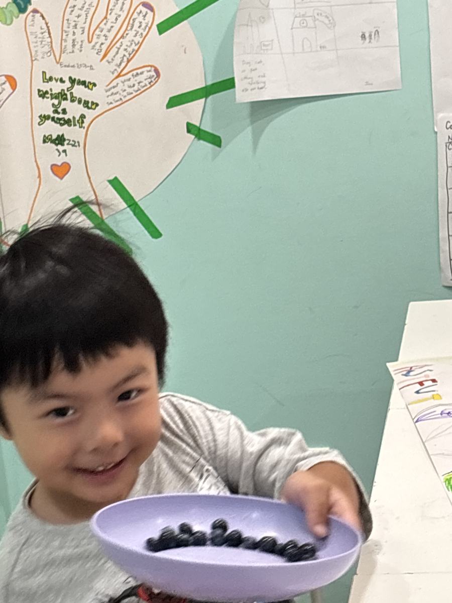 A young student proudly holding out his bowl of blueberries