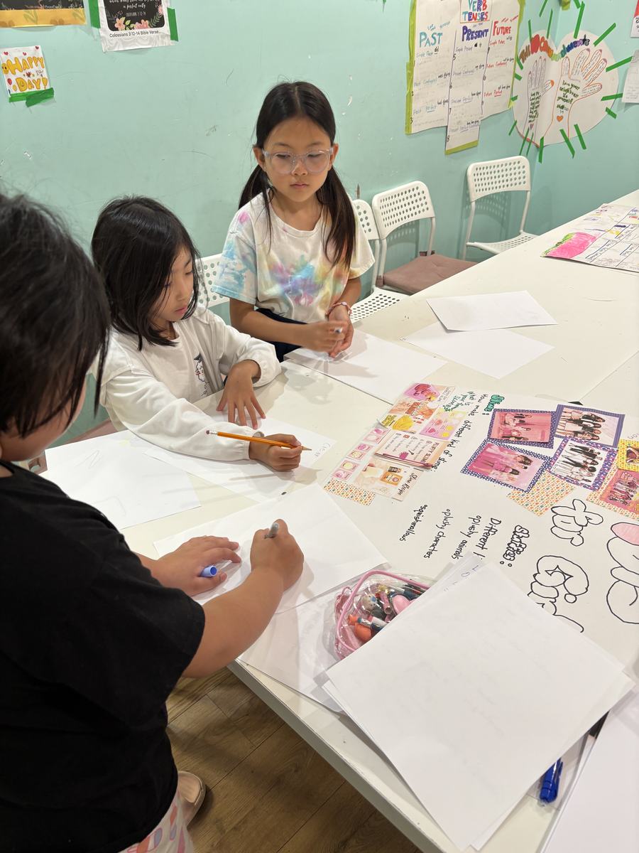 Students working side by side along the table on their posters