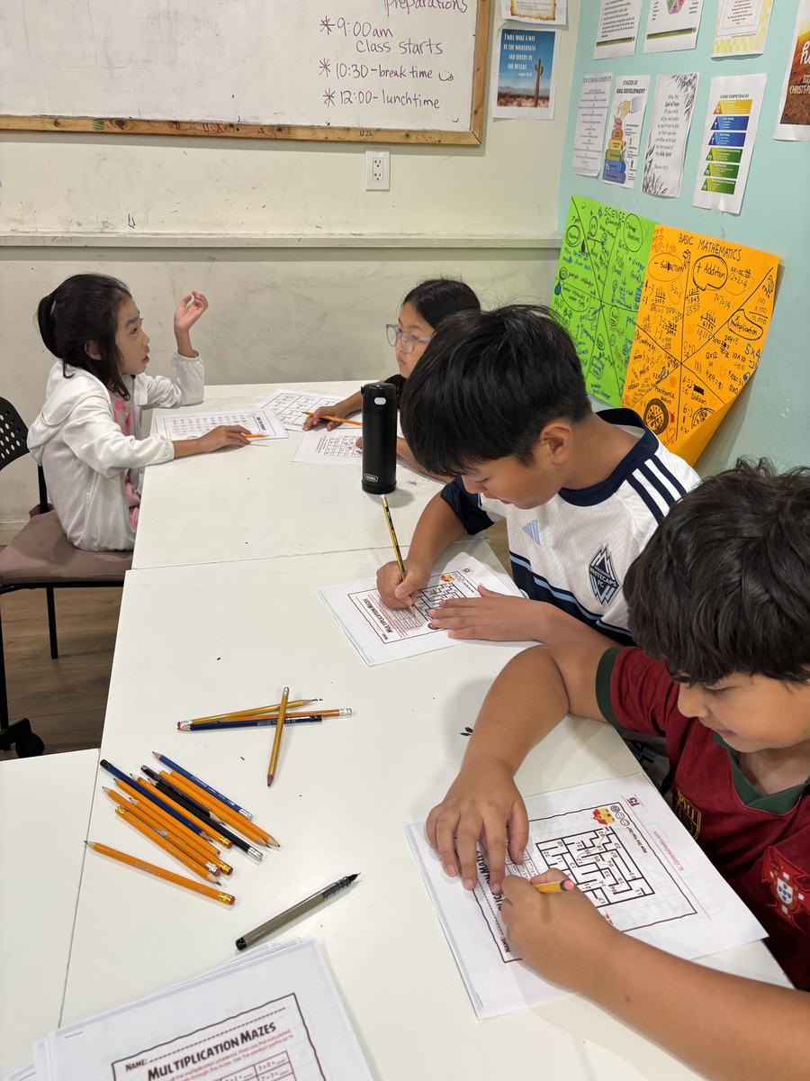Students working at the table with the day's timetable written on the whiteboard behind them