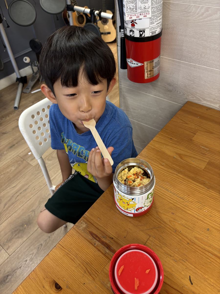 A student eating from his own lunch container with a wooden spoon