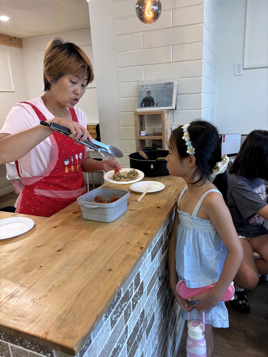 A teacher serving lunch onto a plate for a student waiting at the counter