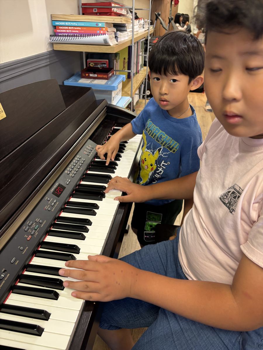 A student playing the keyboard while another watches over his shoulder