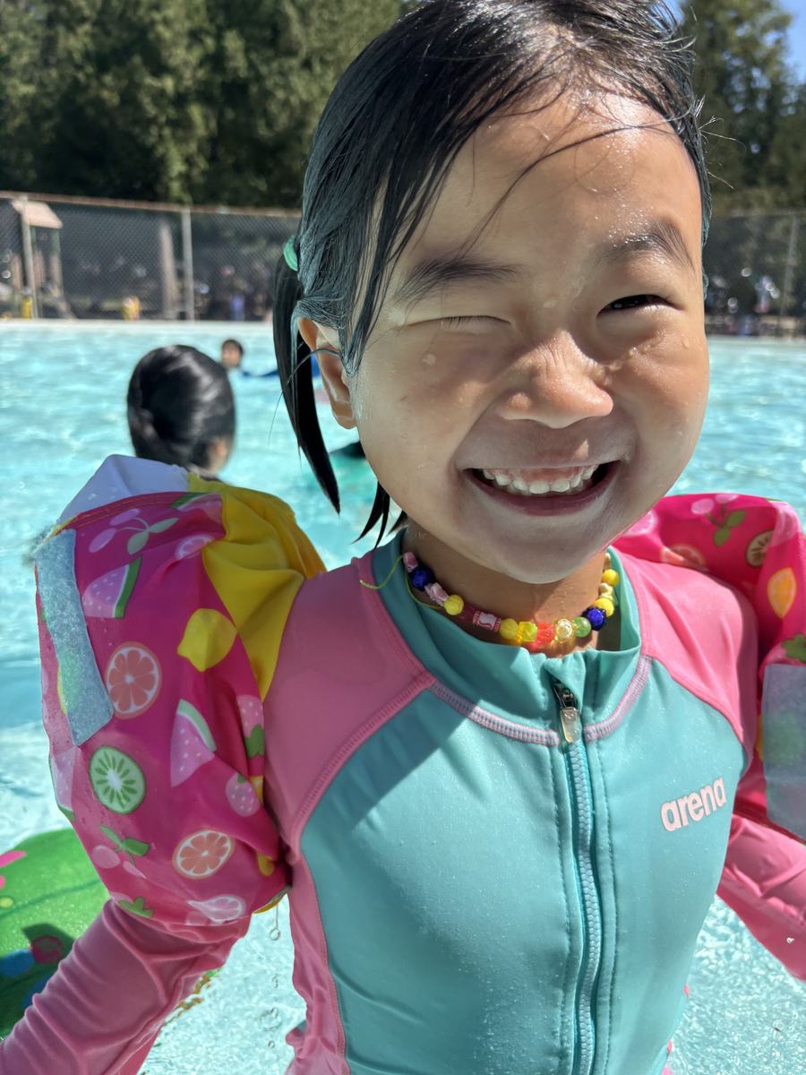 A student grinning at the camera in the water with armbands on