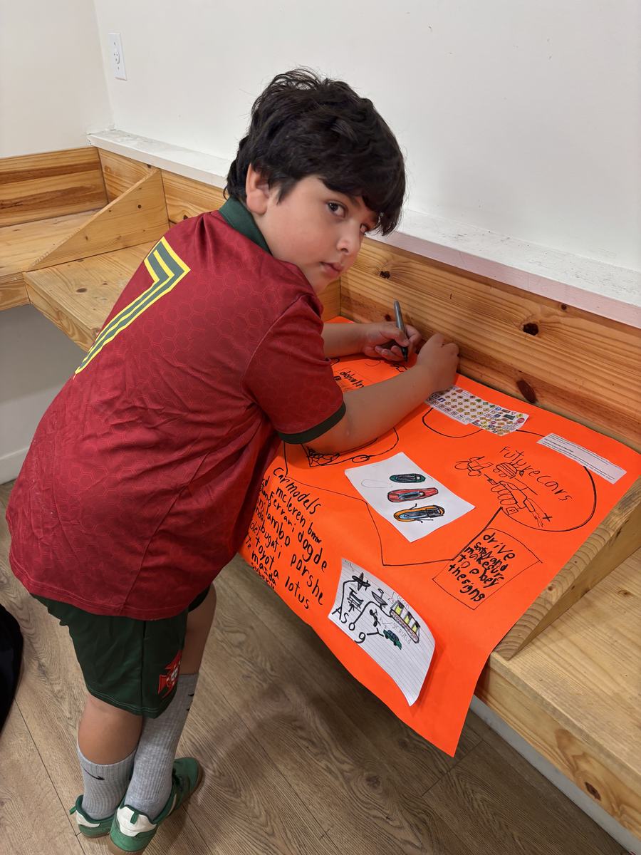 A student writing on his bright orange poster about cars