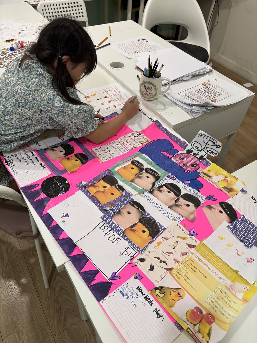 Students working on a poster covered in pink and purple magazine cutouts