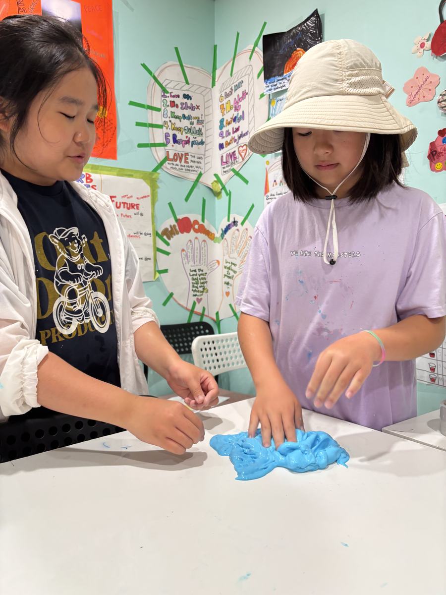 Two students working a batch of bright blue slime on the table