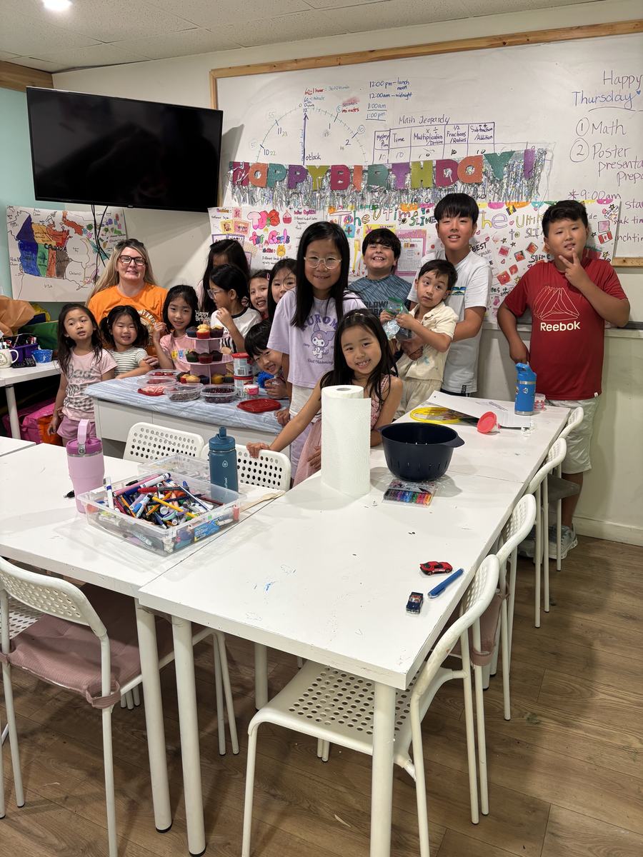 The whole summer camp group and teachers gathered together for a photo in front of the project wall