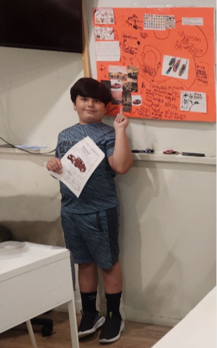 A student standing beside his orange cars poster, holding a labelled car parts diagram