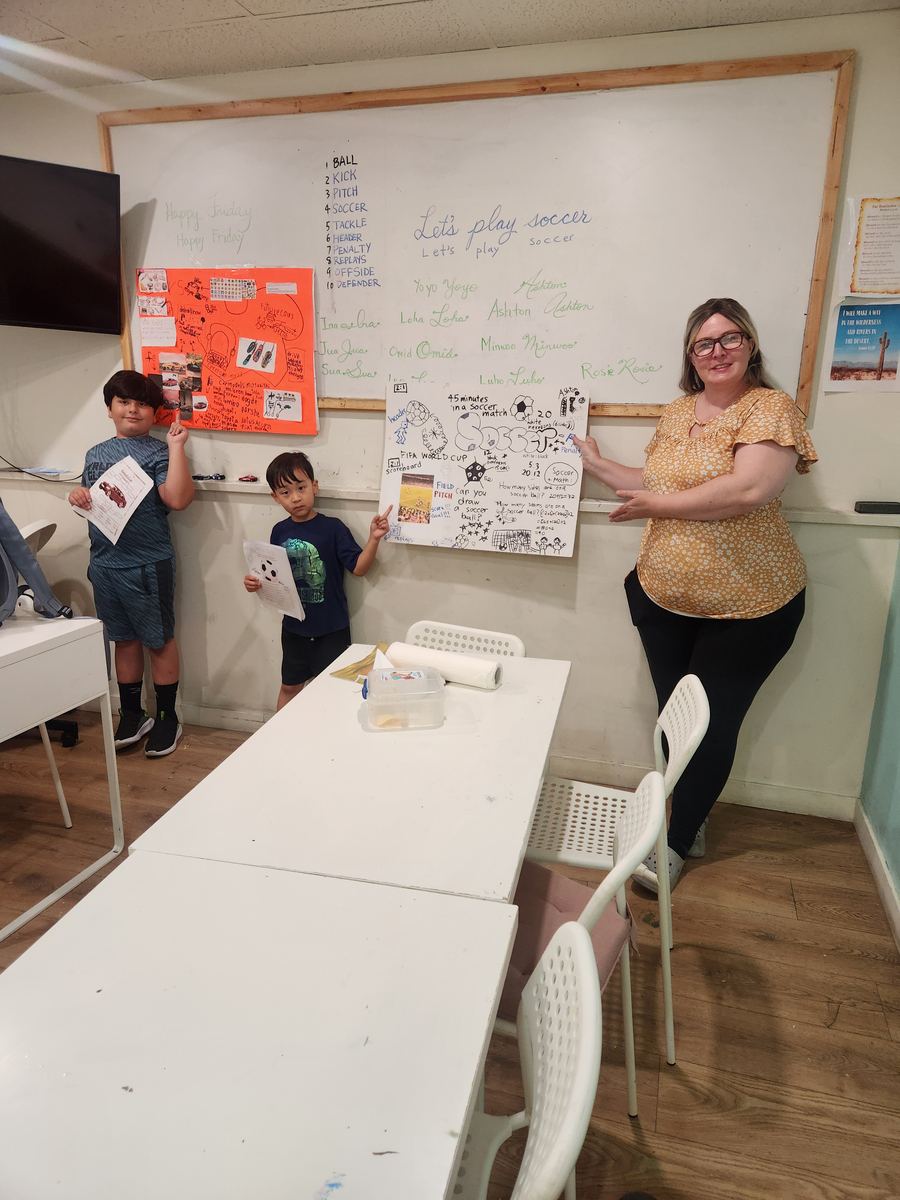 Students standing at the front holding their work while the class watches