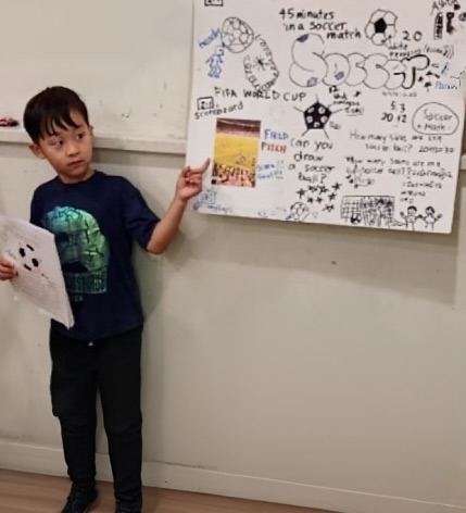A student holding up his completed soccer poster, covered in labelled diagrams and calculations