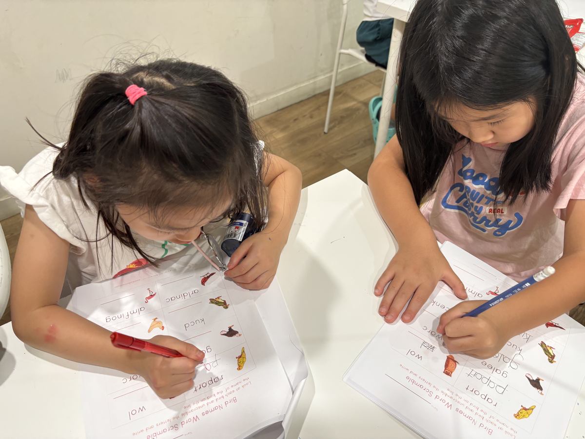 Two younger students colouring and writing at the table together