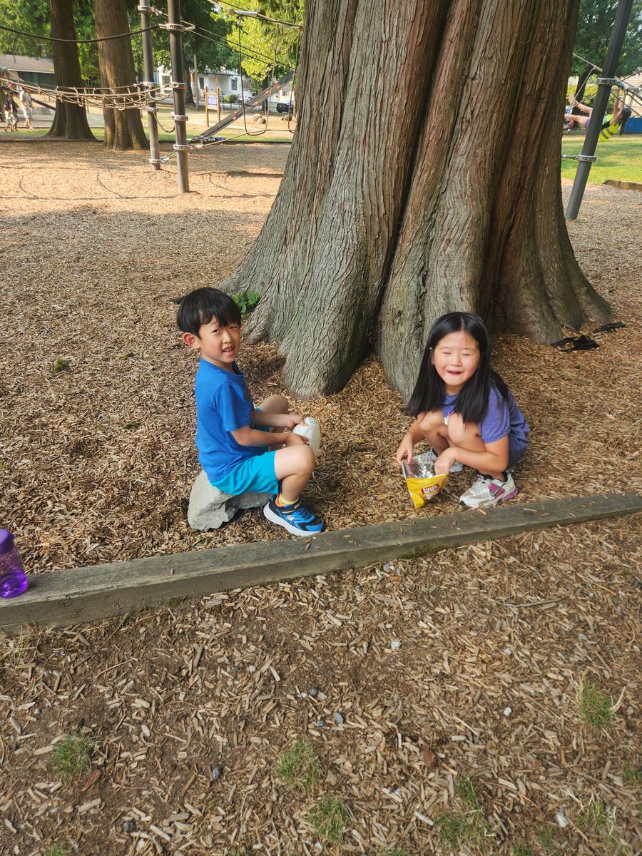 Two students crouched by the tree roots, sharing a snack