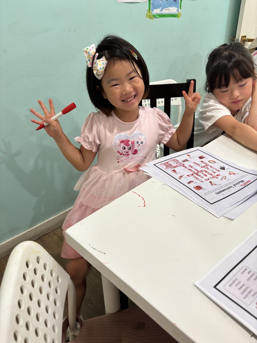 A young student holding up two markers and grinning over her worksheet