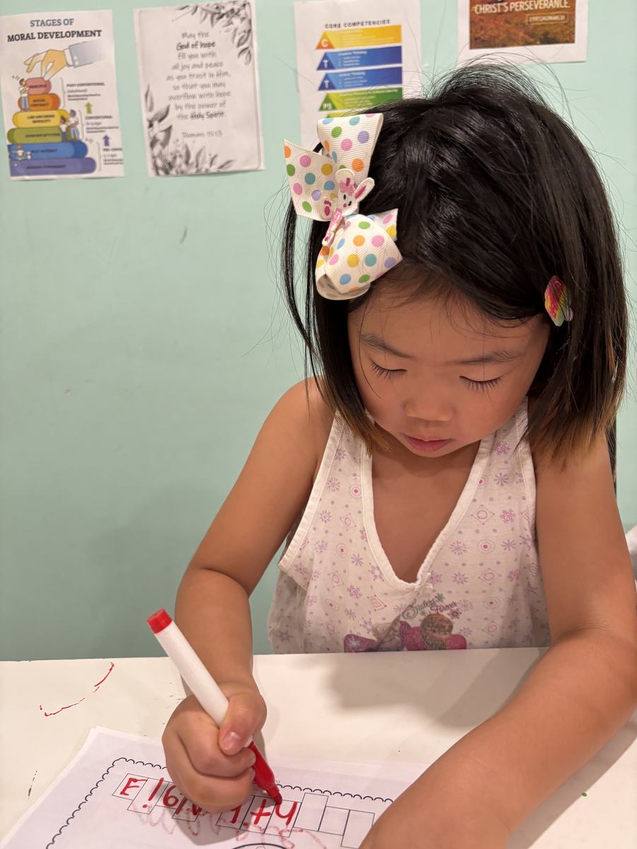 A young student concentrating as she traces letters with a red marker
