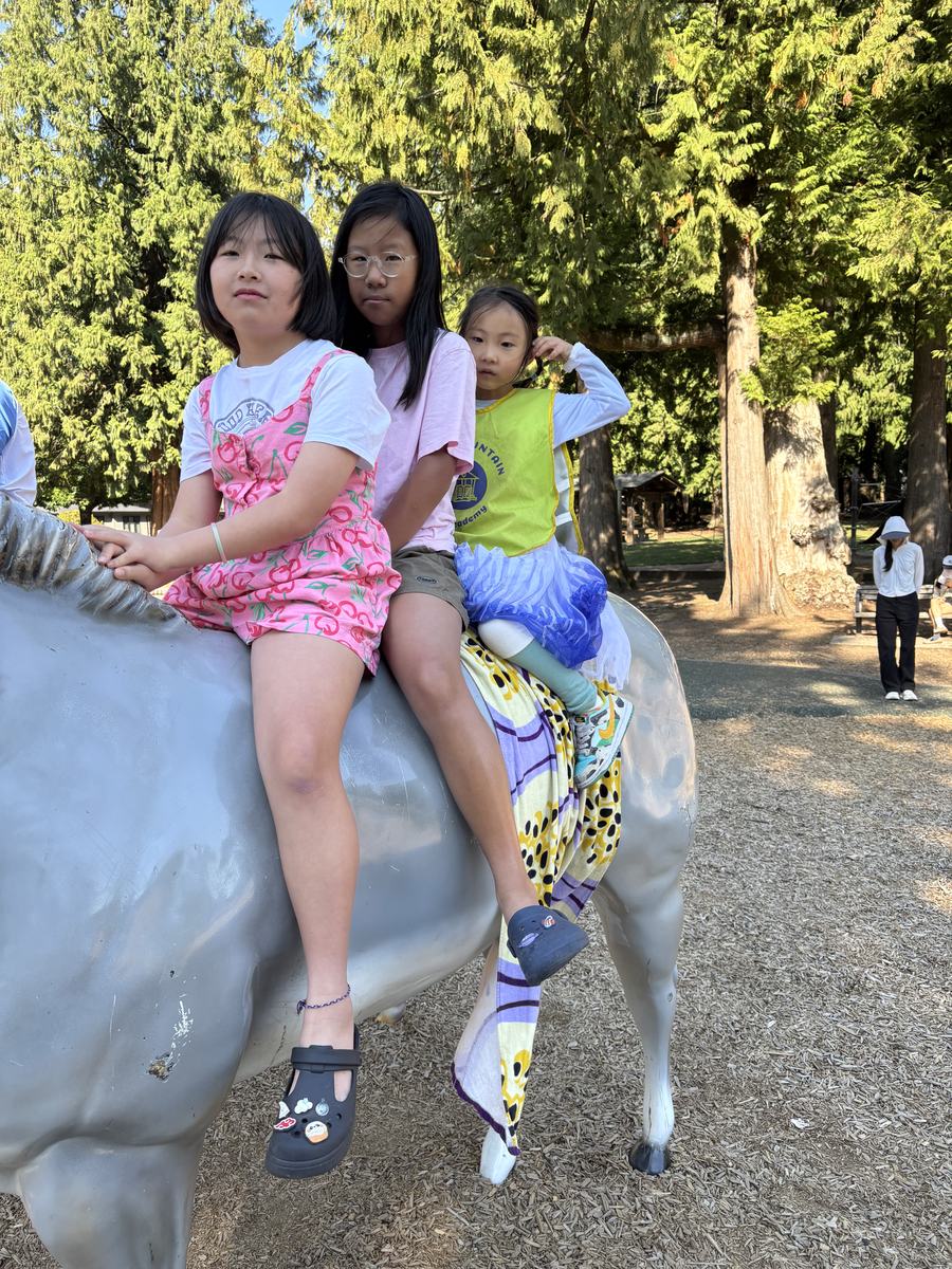 Three girls sitting together on one of the painted horse statues in the park
