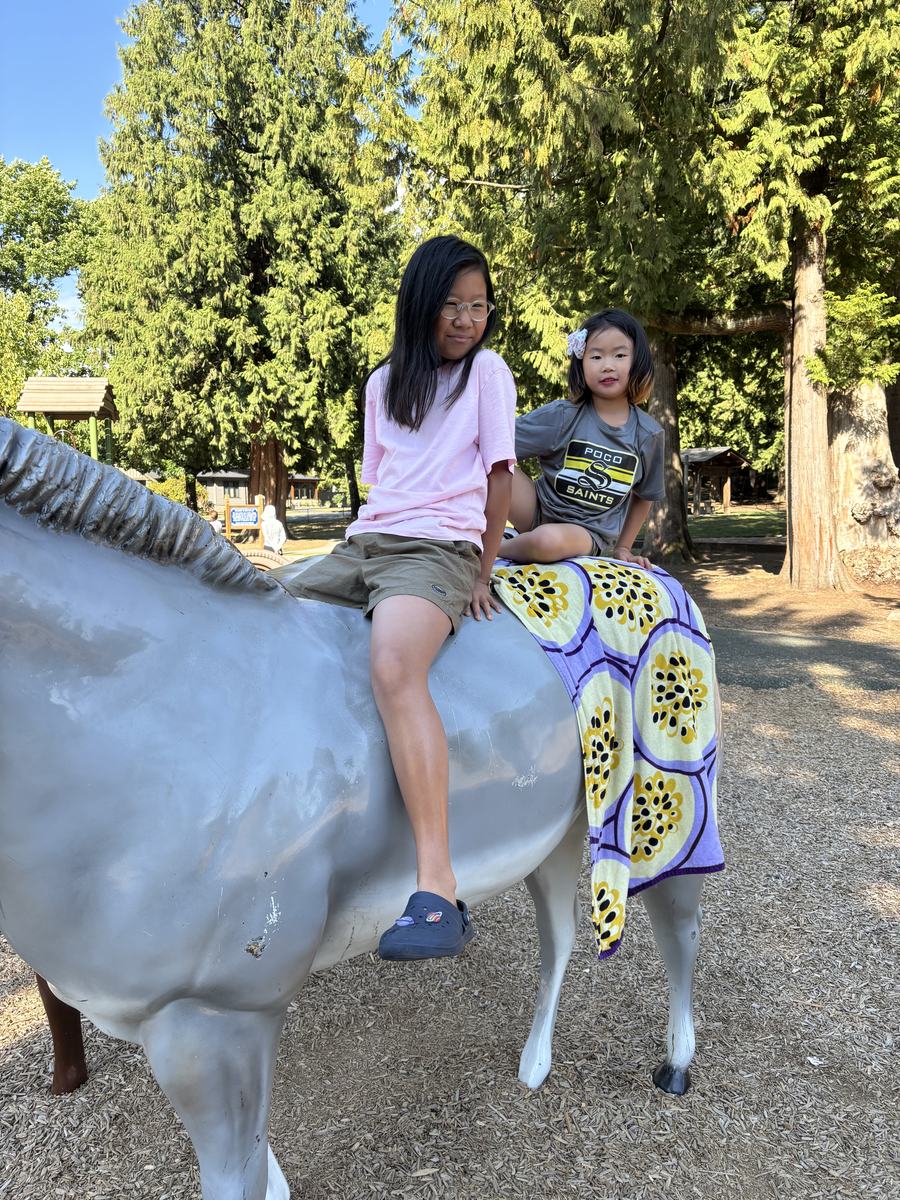 Two students on a painted horse statue under the tall evergreens
