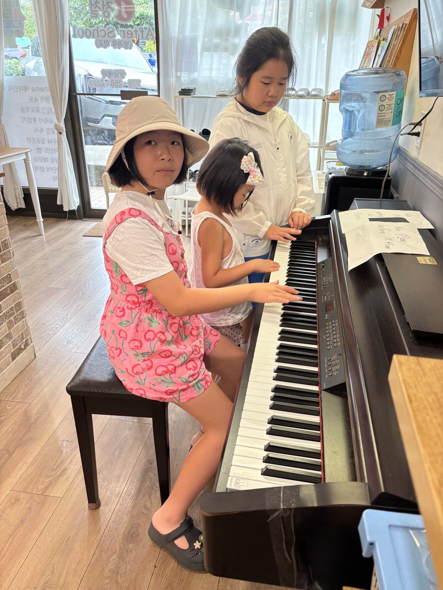 A younger student at the digital piano with two older students helping her find the keys
