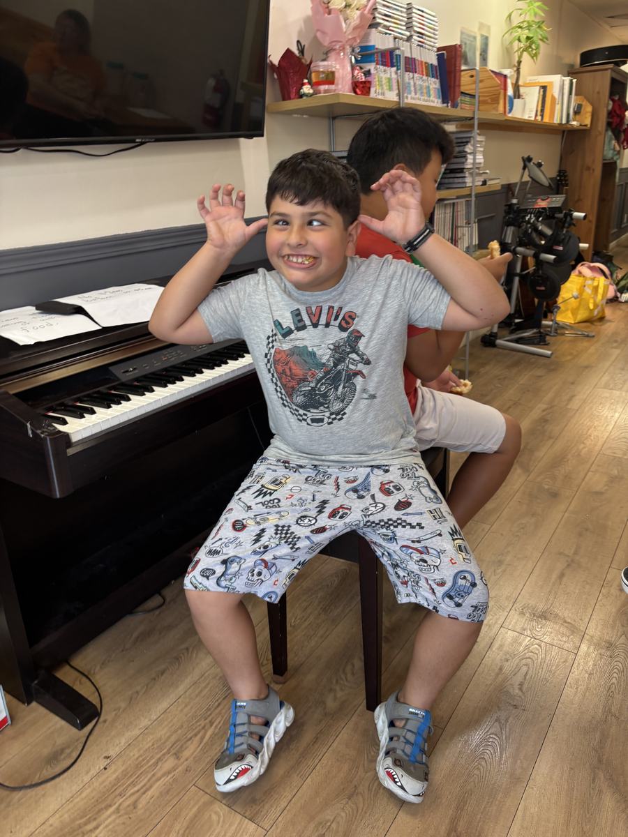 A student sitting at the piano bench with his arms thrown up, laughing