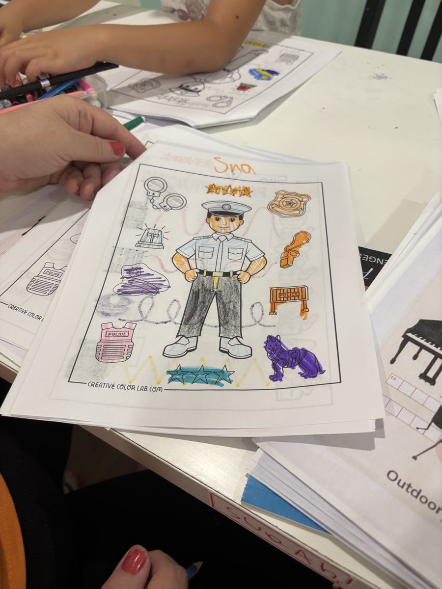A colouring page of an officer in uniform with handcuffs, a badge and a dog, coloured in by a young student