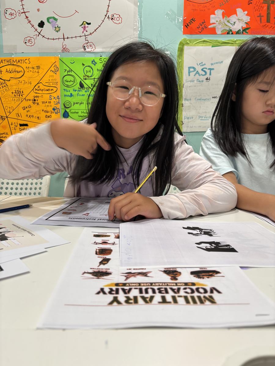 A student smiling and pointing at herself while working on a Military Vocabulary worksheet