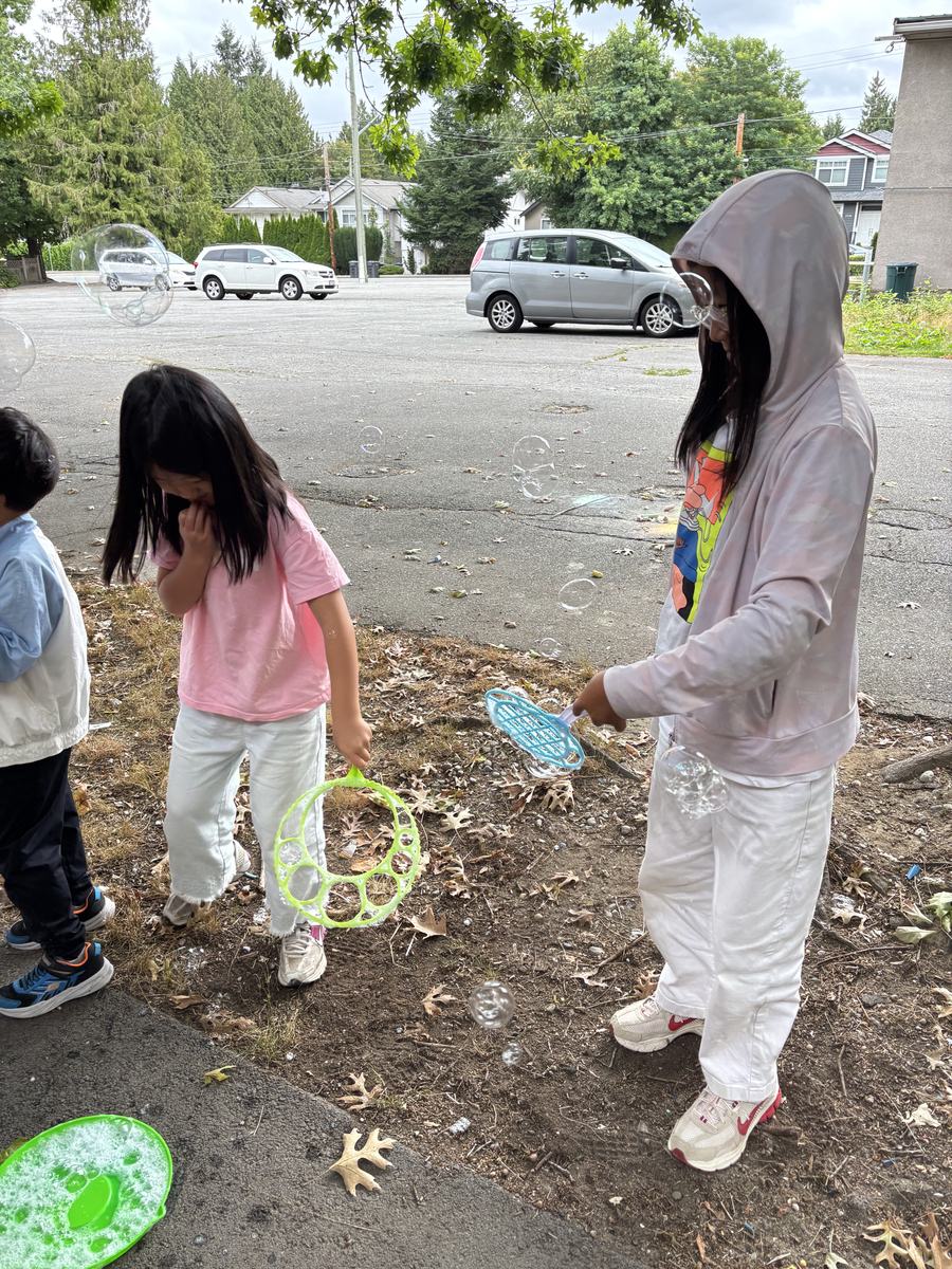 Two students blowing bubbles on the driveway with a pile of bubble wands at their feet