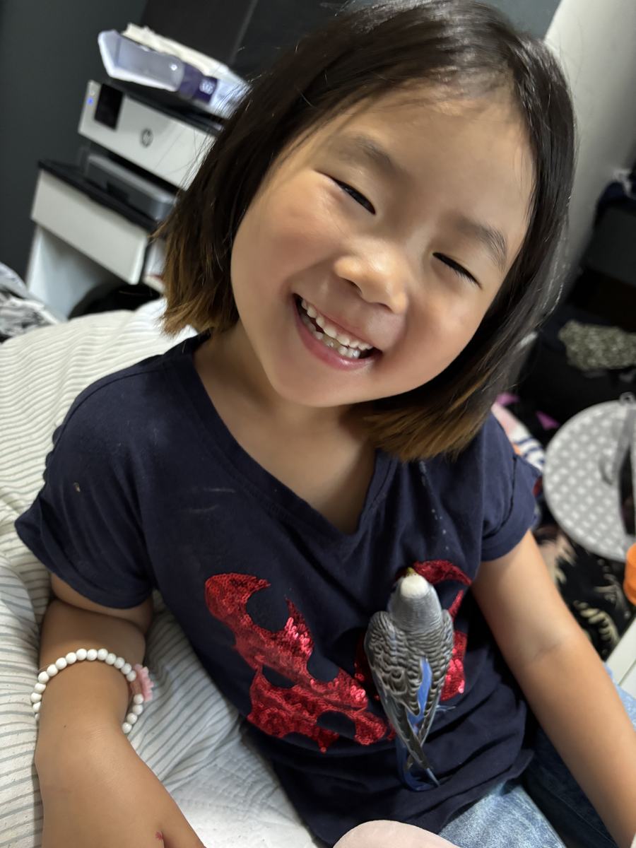 A student sitting on the sofa smiling with a small budgie perched on her shirt
