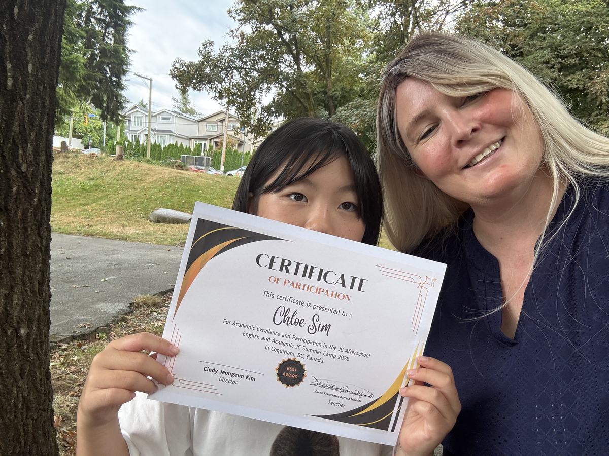 A student holding up her Certificate of Participation while Teacher Diane leans in beside her, both smiling