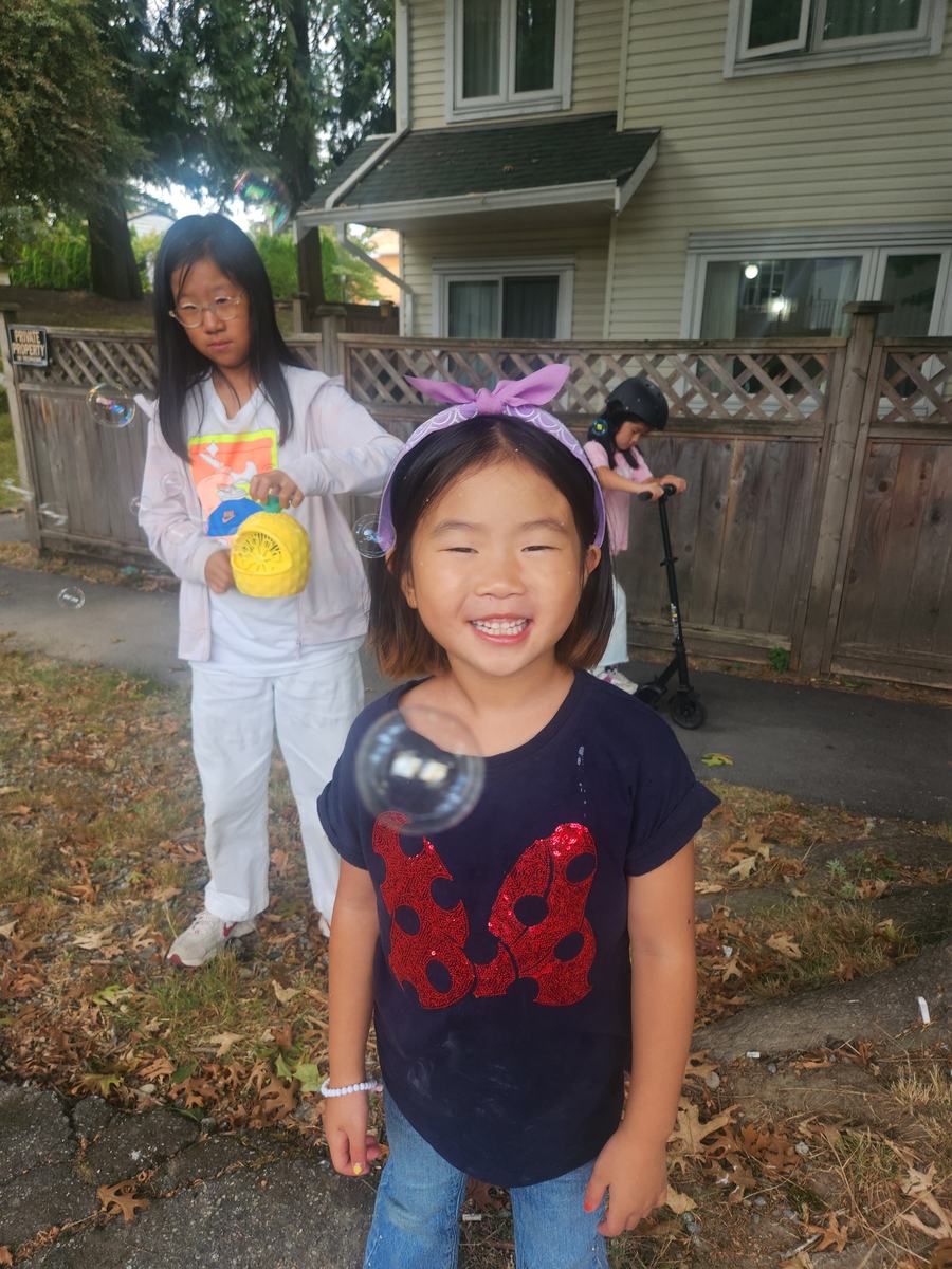 Two students laughing in the driveway, one holding a yellow water balloon