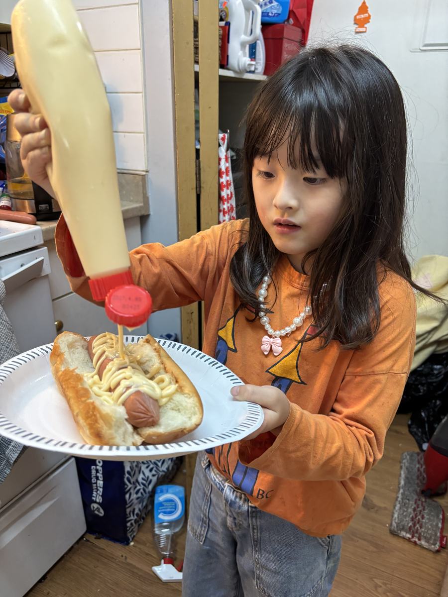 A young student carrying a plate with a hot dog she has just topped with sauce