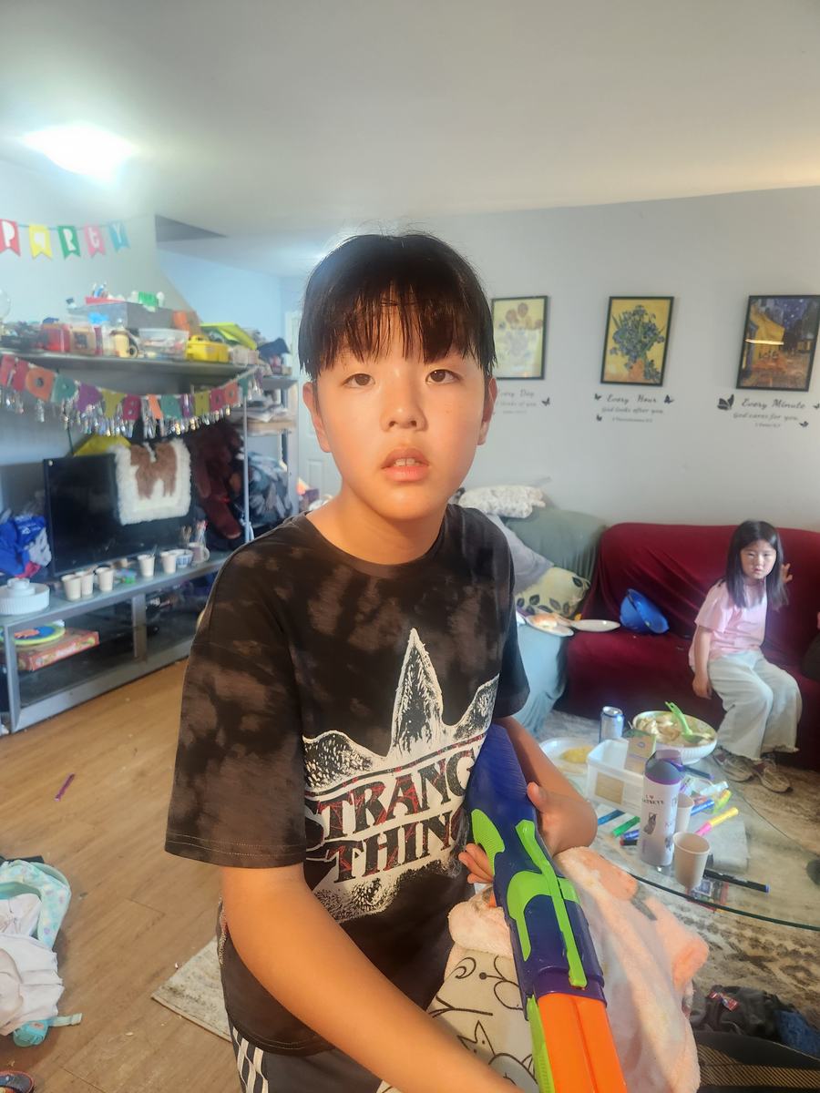 A student standing in the living room holding a water gun, with a party banner and snacks on the table behind him
