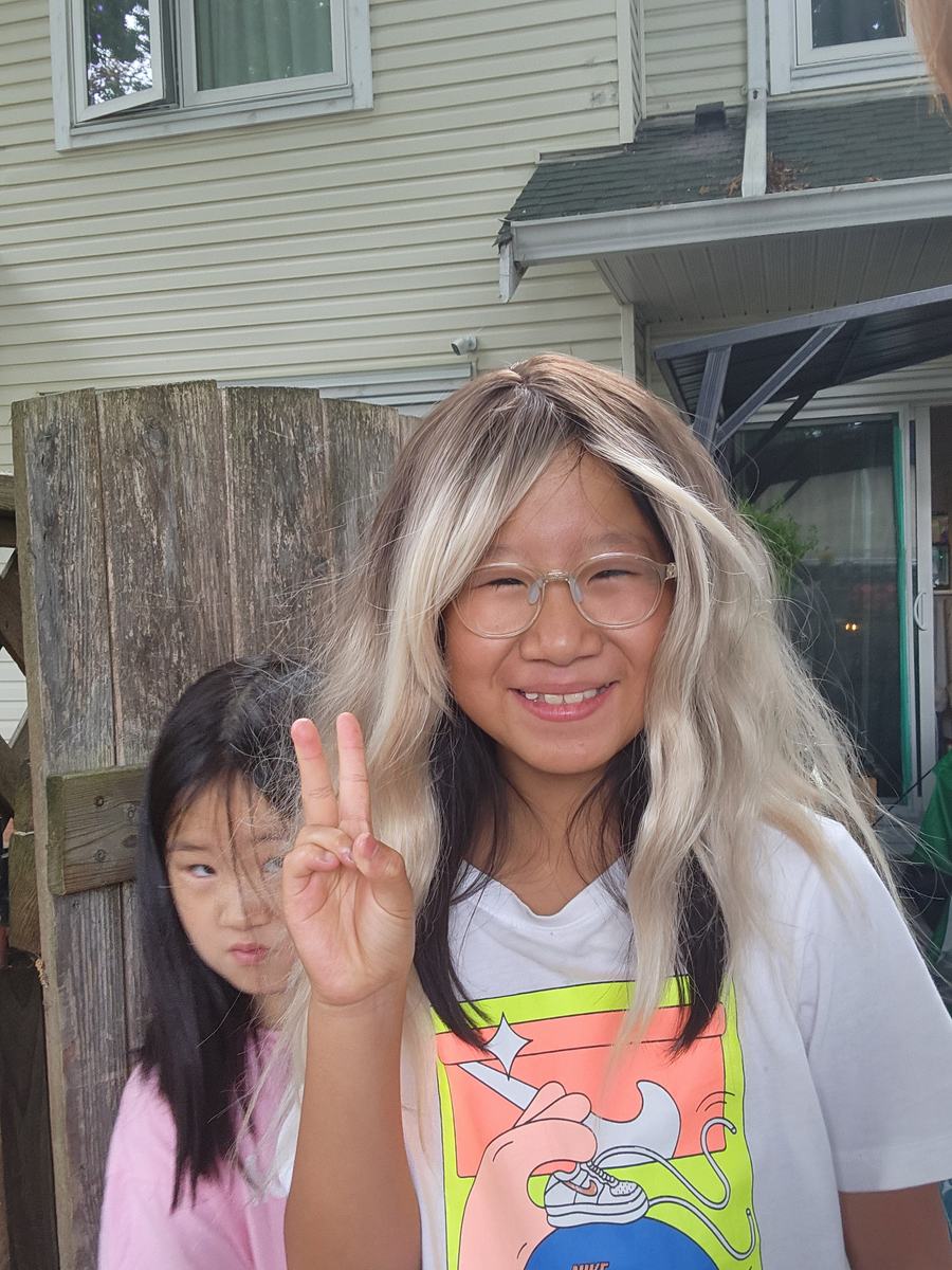 Two students posing for the camera, the older one wearing a long blonde wig, both making peace signs