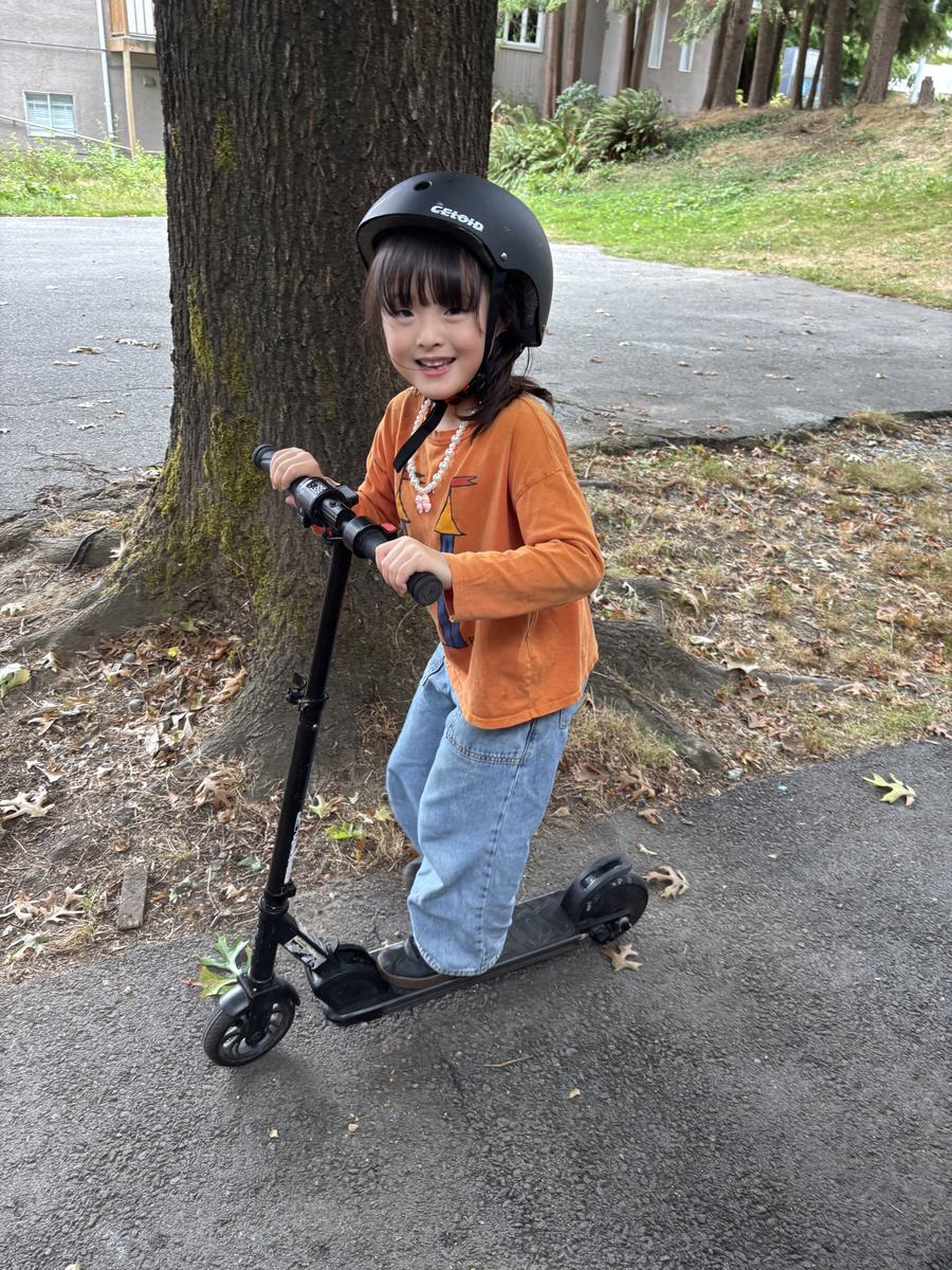 A student in a helmet posing on a kick scooter under the big tree