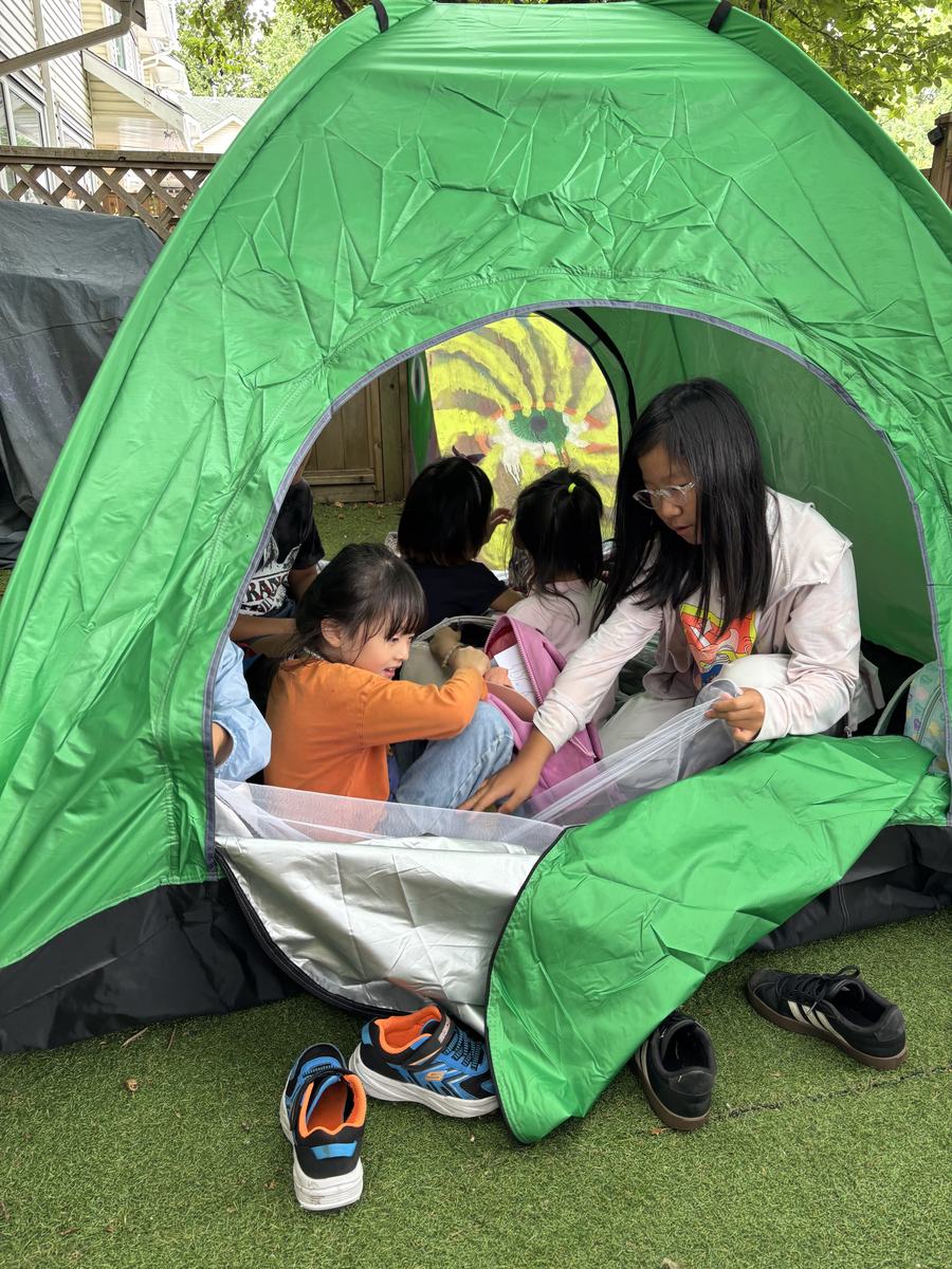 Students crowded inside a green pop-up tent in the backyard, peeking out of the opening