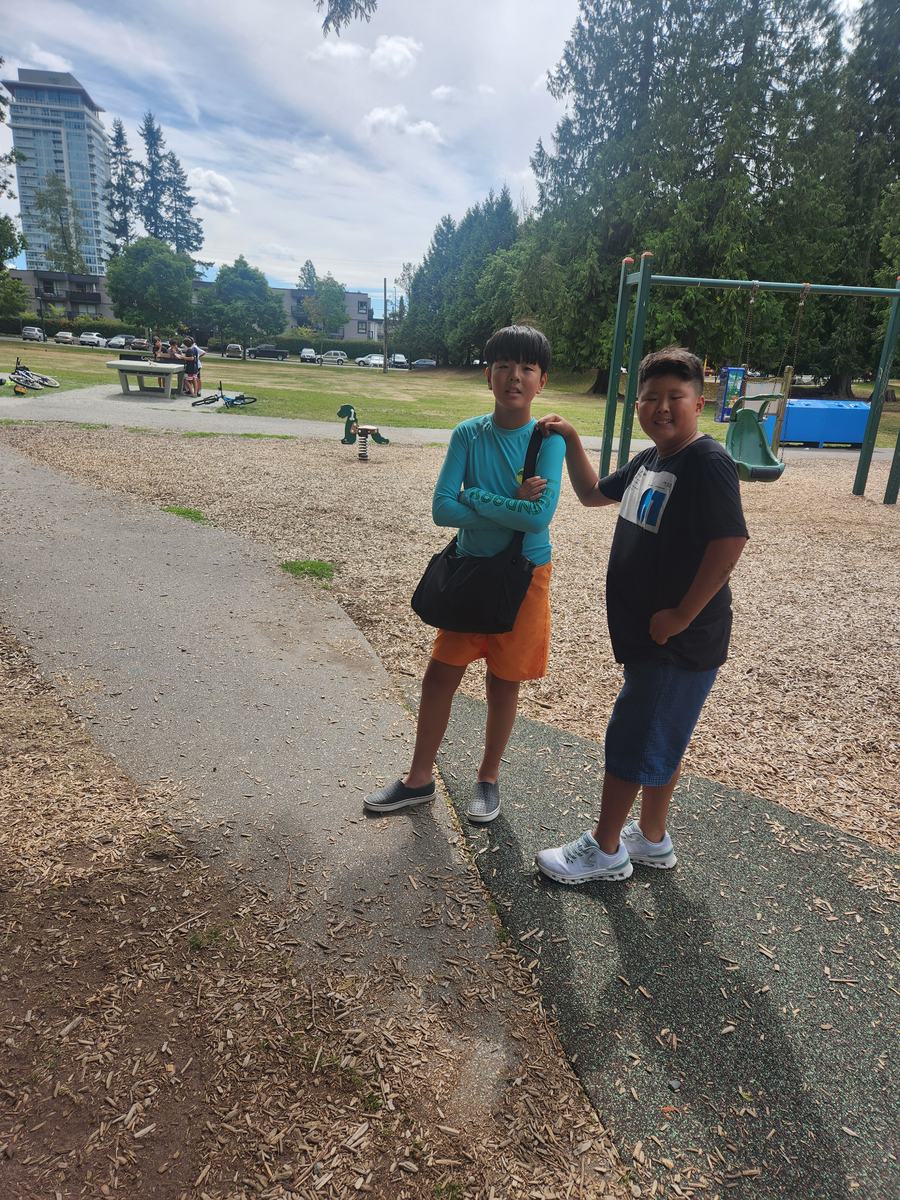 Two students standing together on the park path with the playground behind them