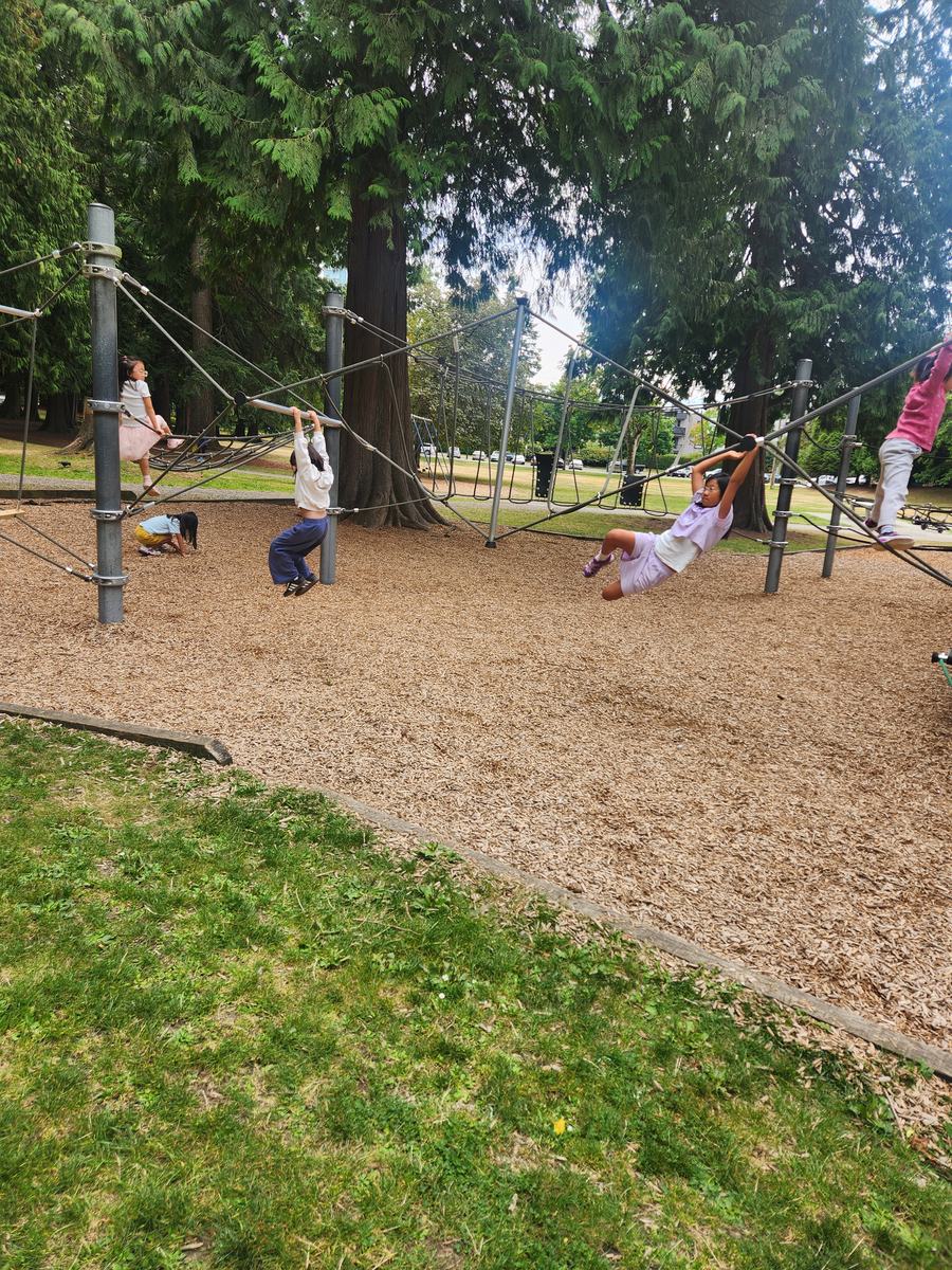 A student hanging upside down from the ropes while others play across the playground