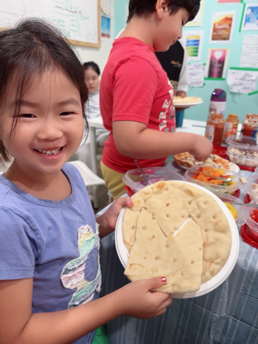 A young camper smiling as she holds up her plain flatbread pizza base