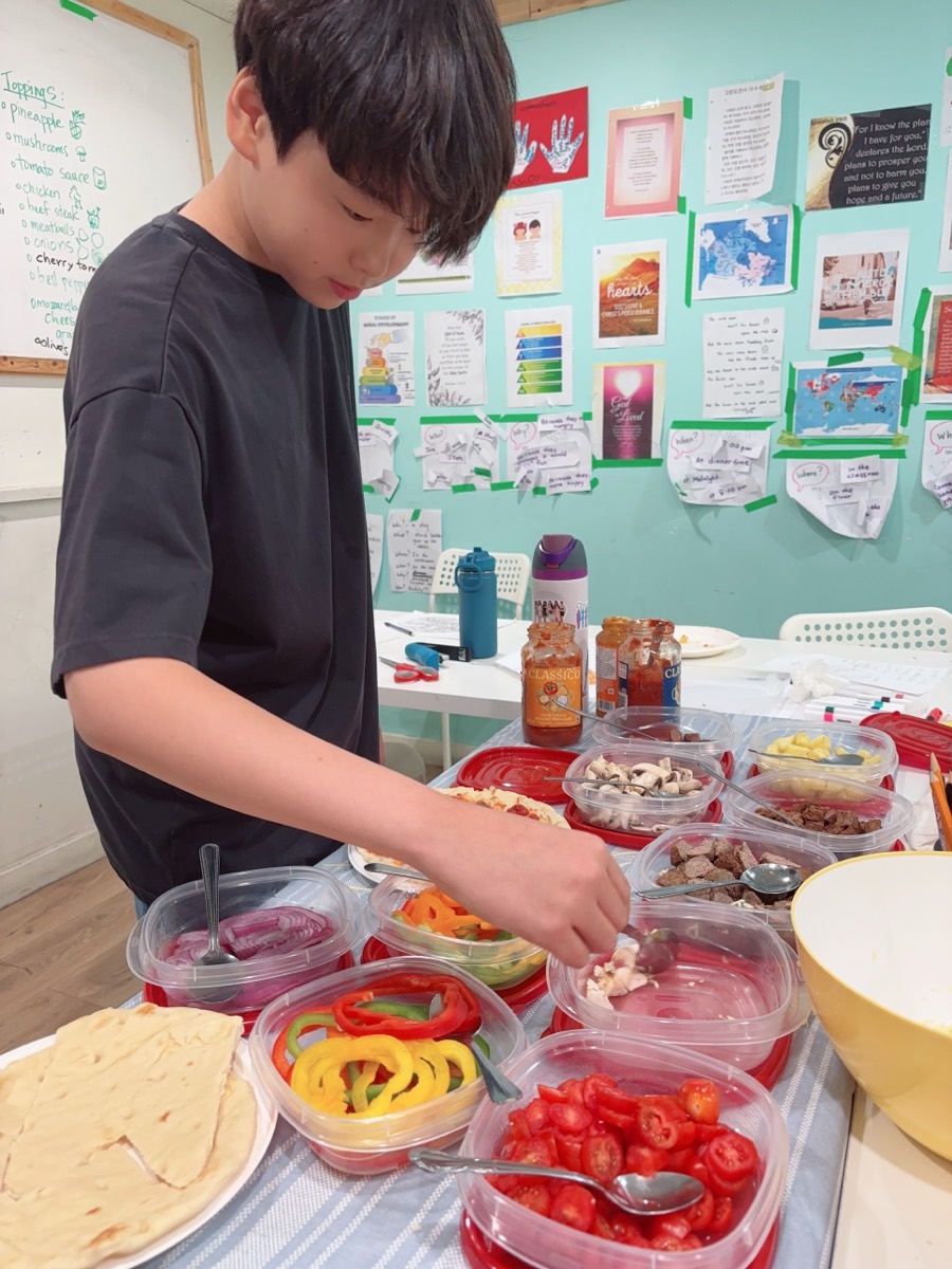 A student reaching across the table to add toppings to his pizza