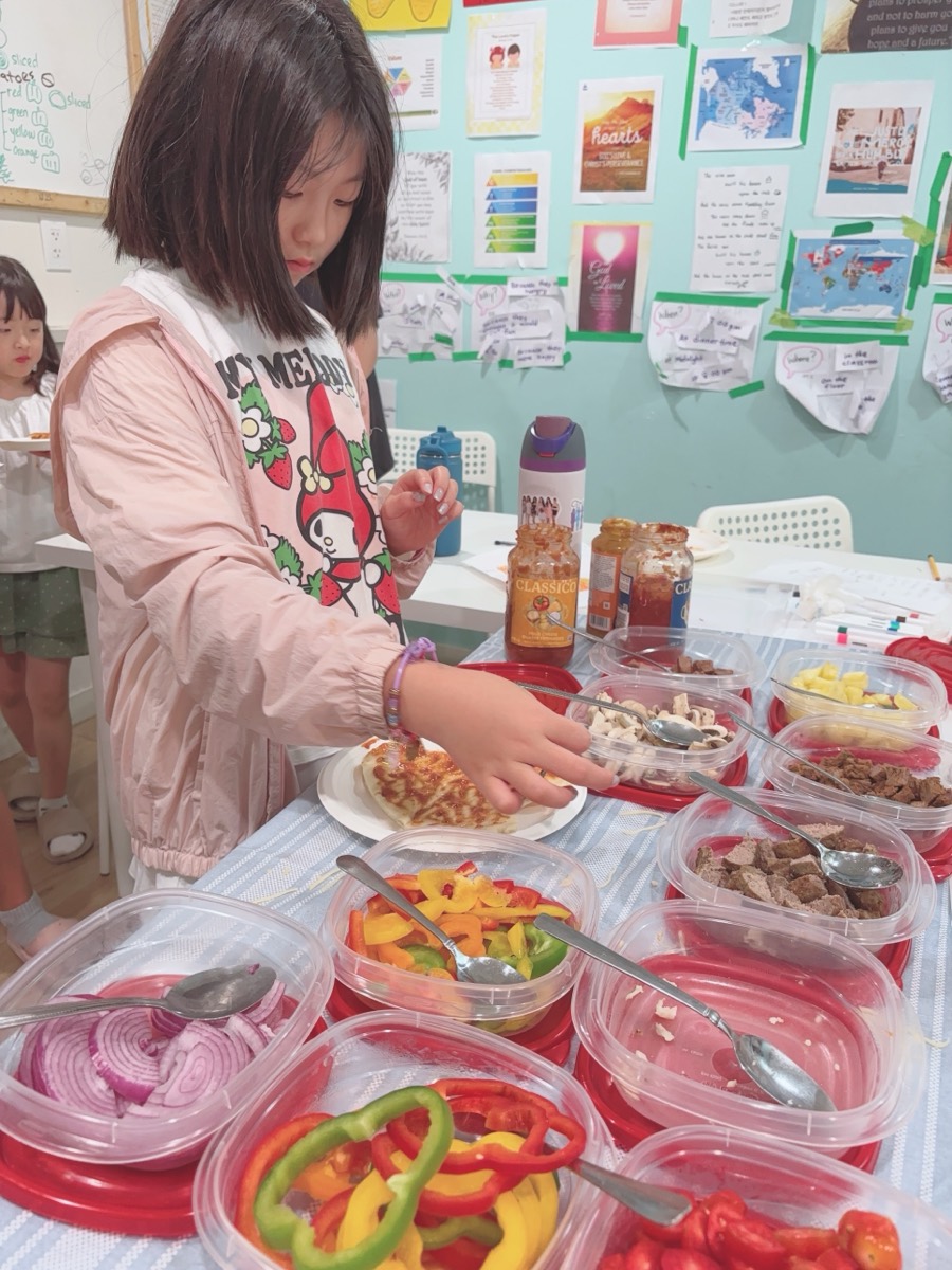 A student carefully placing toppings onto her pizza base