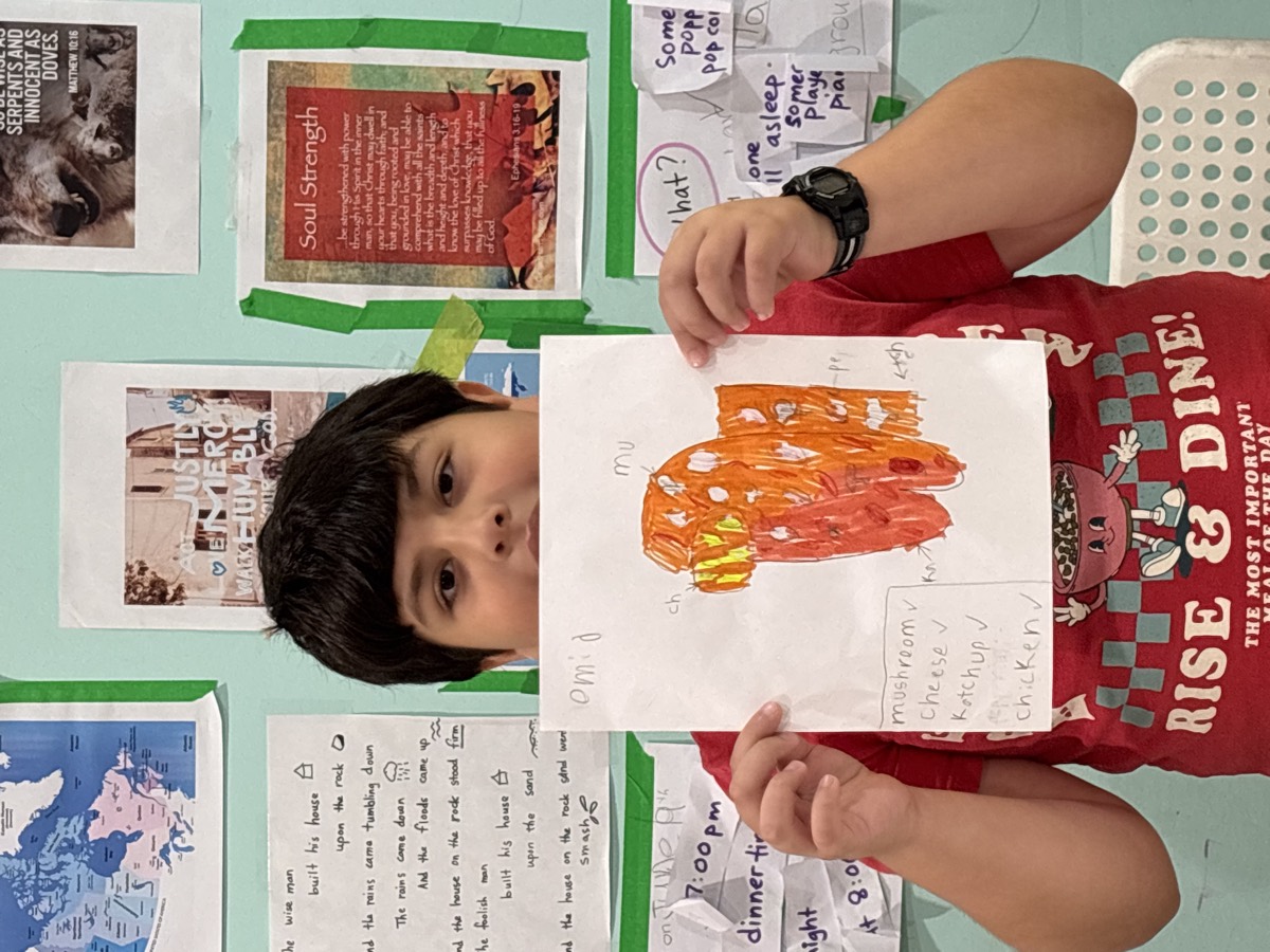 A student holding up his hand-drawn pizza design with a checklist of mushroom, cheese, ketchup and chicken