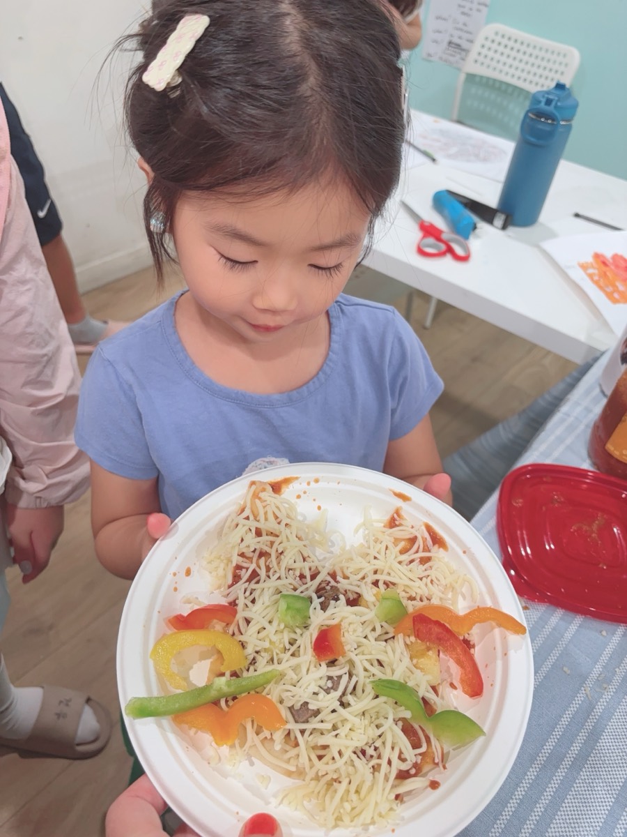 A young student holding a pizza covered in melted cheese and colourful pepper strips