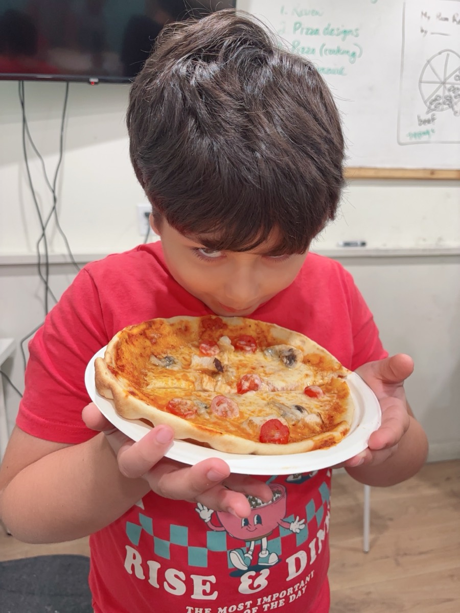 A student presenting his finished pizza on a paper plate