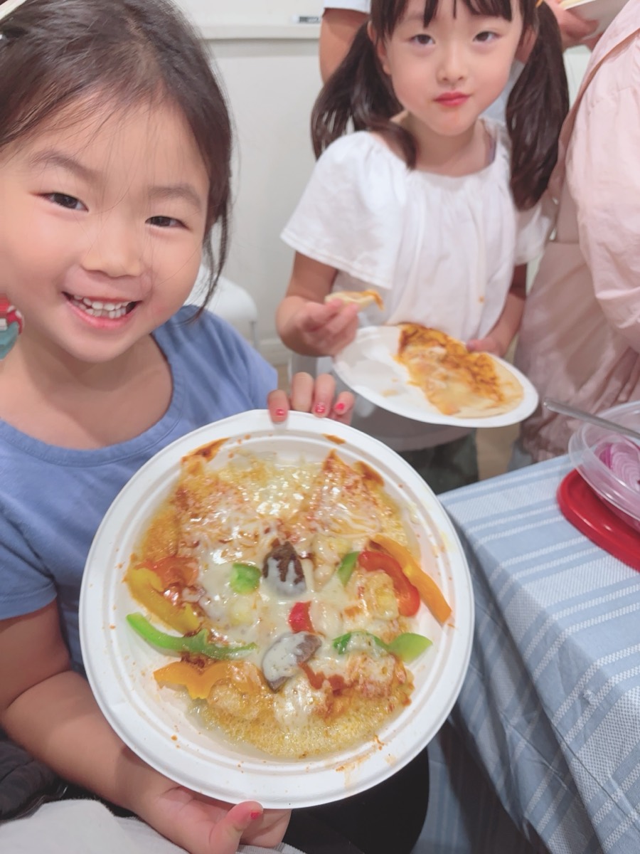 A young camper smiling proudly while holding up the pizza she made herself